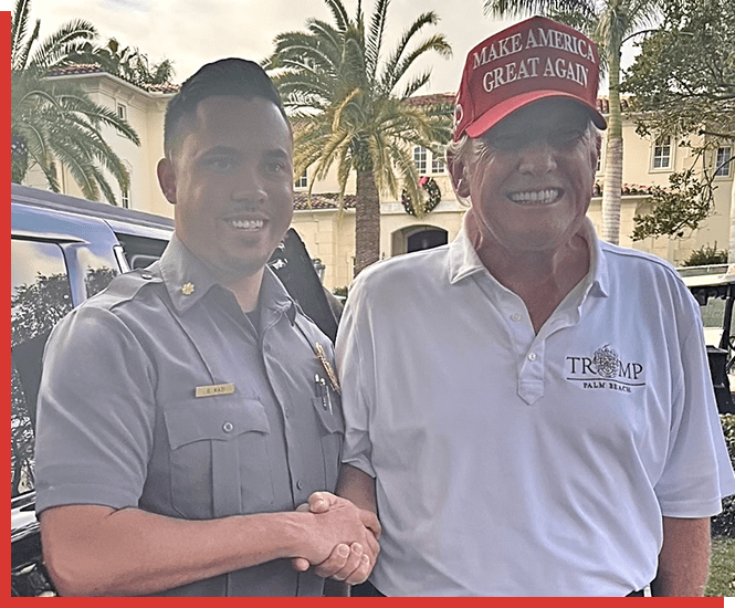 A man and a woman shaking hands in front of palm trees.